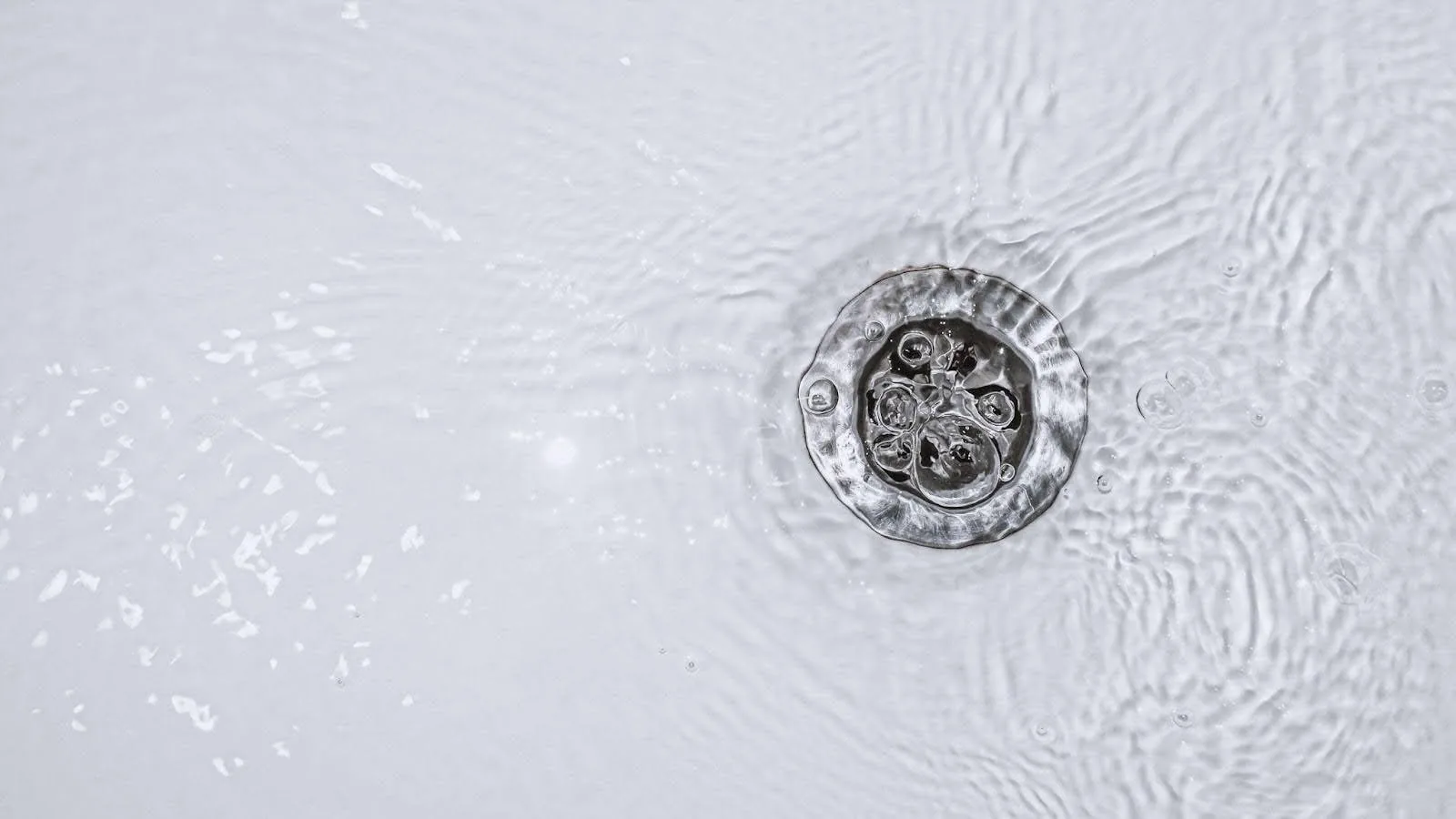 A close-up view of a bathroom drain, showcasing its metallic surface and surrounding tiles