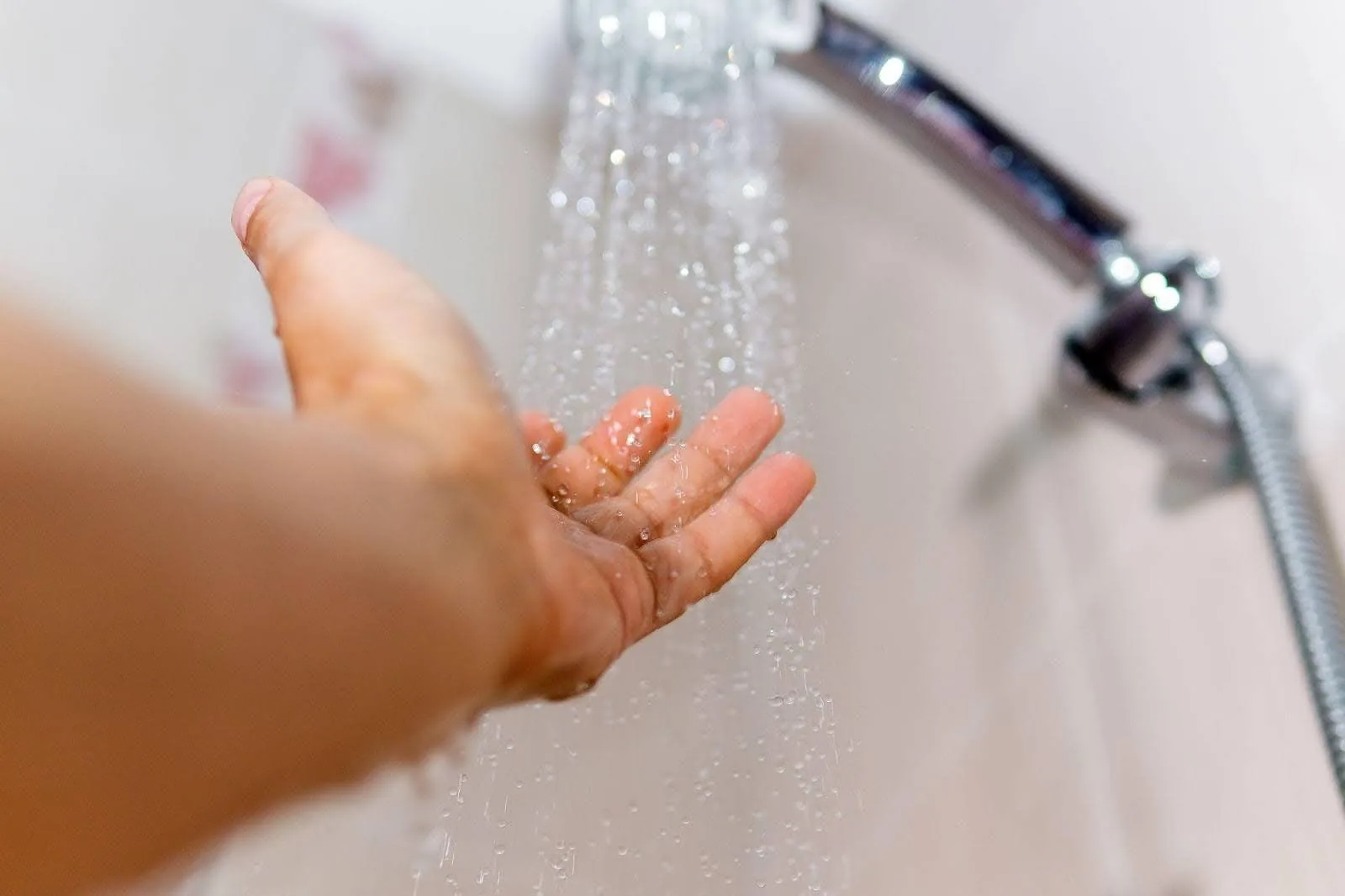 A hand holding a shower head, water streaming out, creating a soothing shower effect