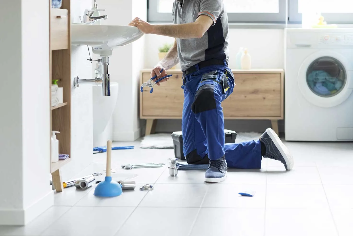 A man in blue overalls repairs a sink, demonstrating practical skills in a home maintenance task.