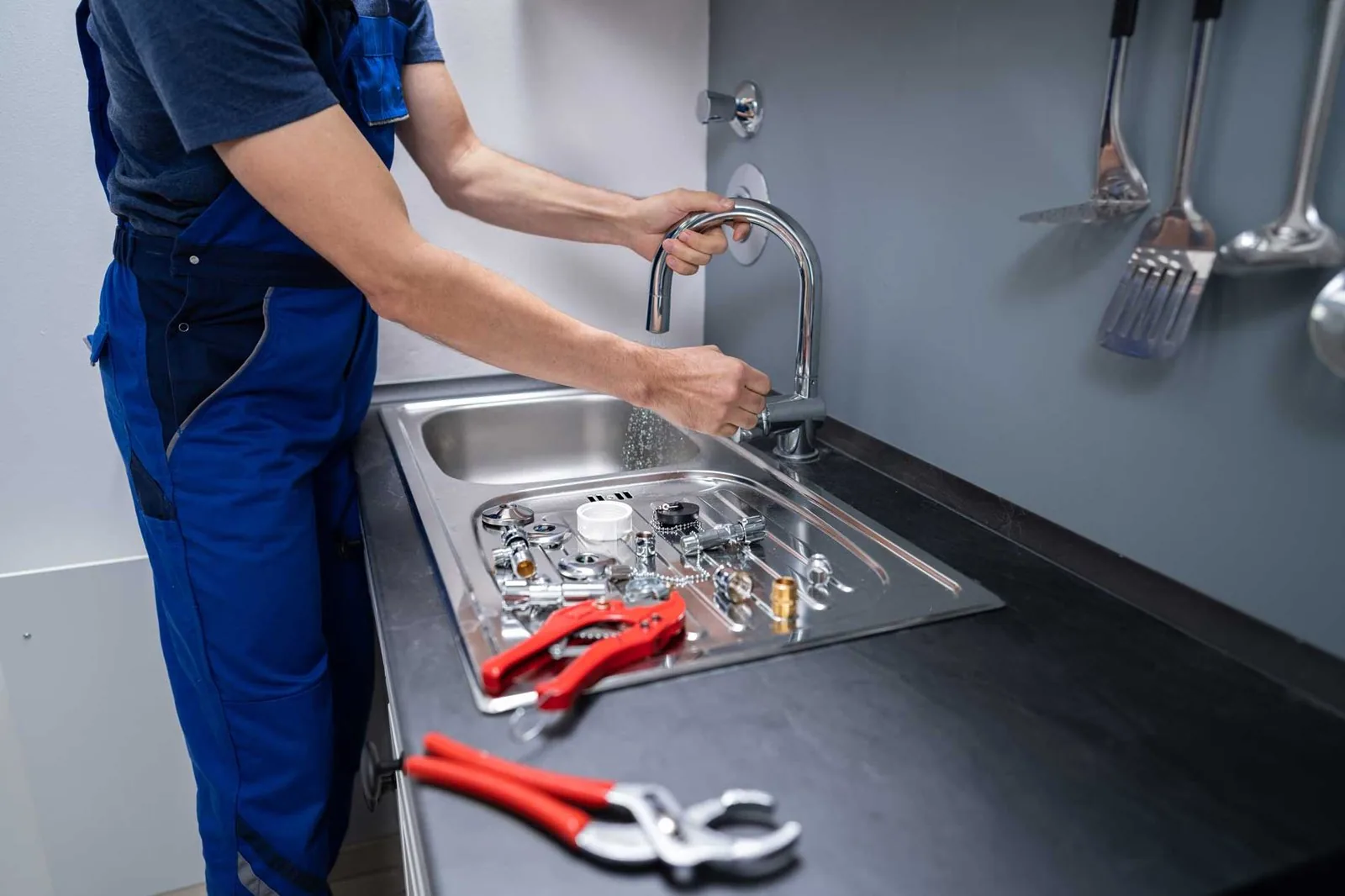 A man in overalls repairs a sink, demonstrating practical skills in a home maintenance setting.

