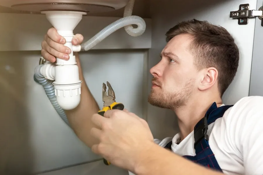 A man using a wrench to repair a sink drain, demonstrating practical plumbing skills and home maintenance.