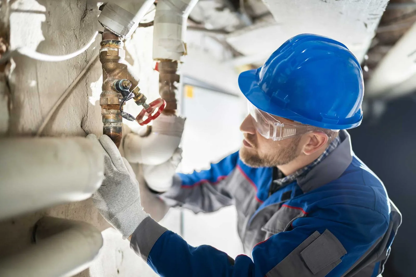 A man wearing a blue helmet and hard hat is engaged in work on a pipe.