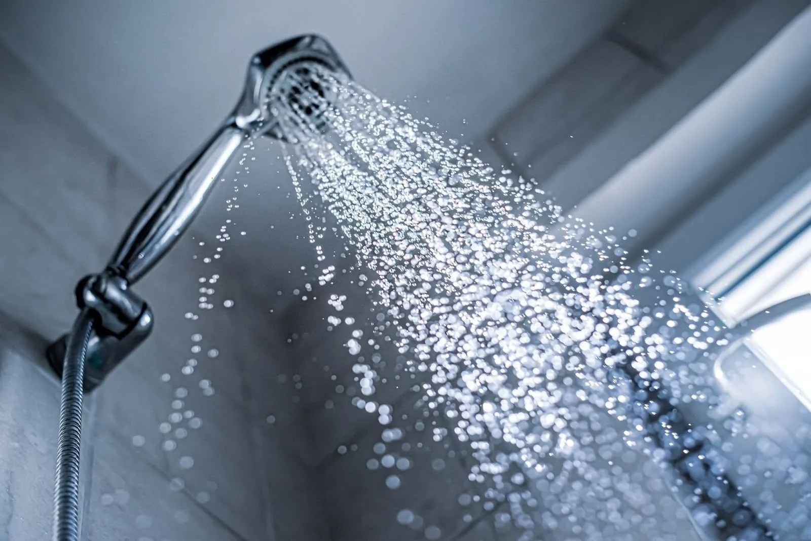 A shower head releasing water,illustrating the difference between low and normal water pressure in a bathroom setting.