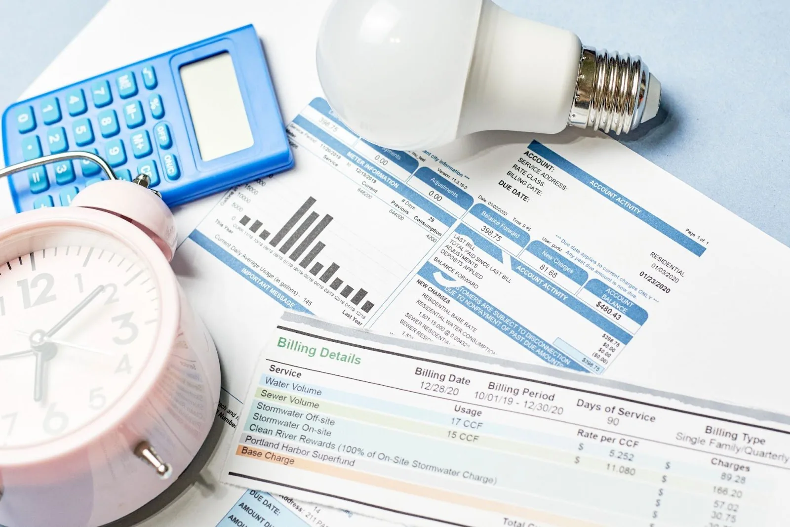 Pink alarm clock, calculator, and light bulb on financial documents. Local plumbing service, leak repairs, repair services.